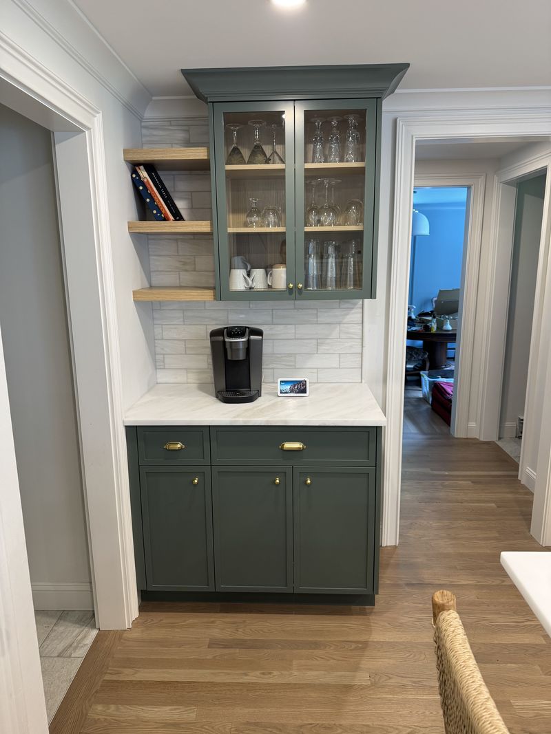 Custom green coffee bar with glass-front cabinets and floating shelves