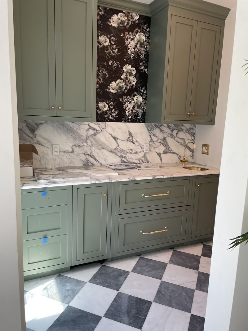 Custom sage green butler's pantry with marble backsplash and brass hardware